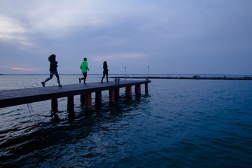 group of young people training outdoors, runners exercises, sea or river background 