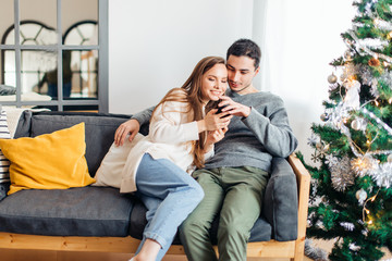 Young couple for Christmas eve hugging lying and looking at cell phone