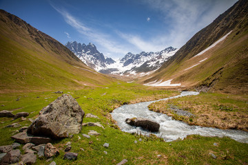 Summer landscape with river and mountain snowy peak, Kazbegi national park, Georgia. The main Caucasian ridge. Green hills and small mountain river in Caucasus foothills, above view
