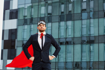 Businessman in a superman costume against a business building background.
