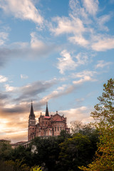 Basilica of Santa Maria la Real de Covadonga, Asturias, Spain, Europe. Beautiful scenery of touristic travel destination in an autumn sunset with a vibrant colorful sky and green forest in mountains.