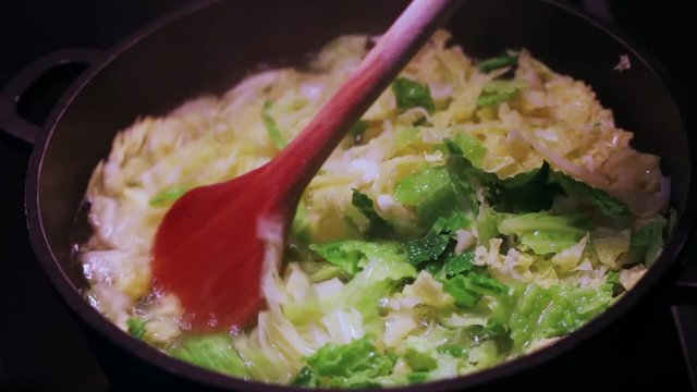 savoy cabbage cooking in the saucepan on the stove top with wooden spoon 