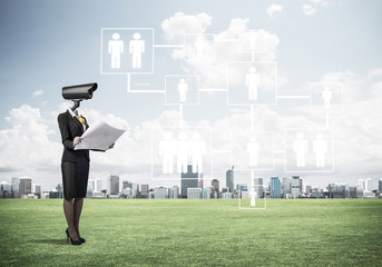 Camera headed woman standing on green grass against modern citys