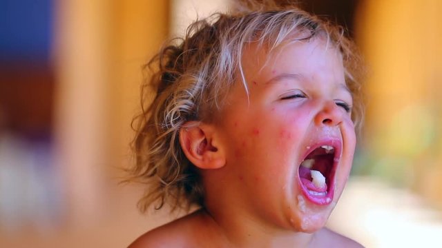 Candid moment of infant boy opening mouth wide open. Toddler baby acting goofy by drooling with food spitting fruit