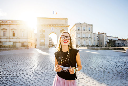 Portrait of a young happy woman tourist with photo camera in front of the famous Triumphal Arch during the morning light in Montpellier city, France