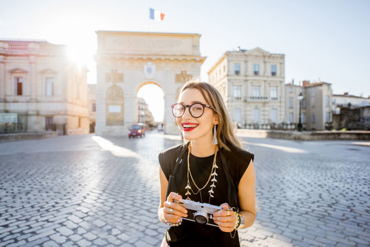 Portrait of a young happy woman tourist with photo camera in front of the famous Triumphal Arch during the morning light in Montpellier city, France