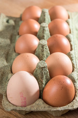 Close-up view of raw chicken eggs in egg box on  oak wooden background