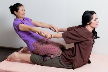 Asian massagist doing thai massage for caucasian woman in spa salon