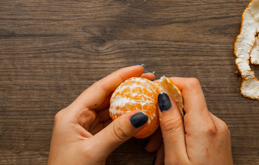 Woman hand peeling ripe sweet tangerine. on a wooden background. with copy space. top view