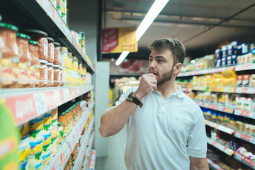 A man thinks what kind of product in a supermarket to choose. The buyer selects canned food at the store. Shopping in a supermarket.