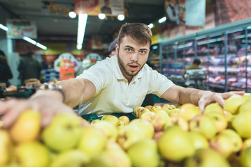 The Emotion man picks up apples in a supermarket and looks at the camera. Shopping for a supermarket.