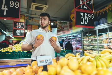A funny young man is played by the apes in the supermarket and looks at the camera. Purchase fruit at the store. Shopping in the supermarket.