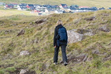 woman with a backpack walks on the hills on the Faroe Islands