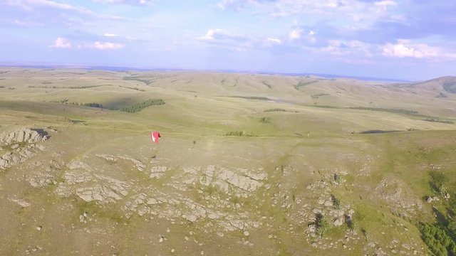 AERIAL: The paraglider flies along the rocky mountains. The paraplane swayed in the wind. Amazing landscape of endless mountains at sunset.