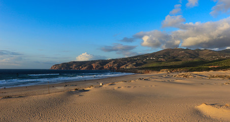 Sunny beach with sand dunes and blue sky and a mountain in background. Guincho beach in Cascais Portugal