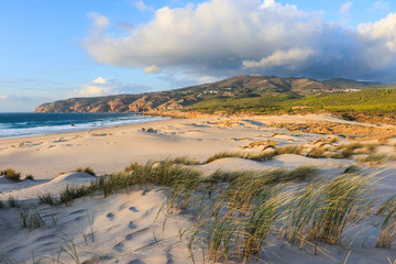 Fototapeta na wymiar Sunny beach with sand dunes and blue sky and a mountain in background. Guincho beach in Cascais Portugal