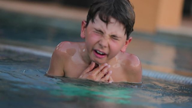 Child pretending to be choking at the swimming pool. Dramatic shot of young boy pretending to be in trouble. Child in distress doing cry-wold seeking attention in super slow-motion 120fps
