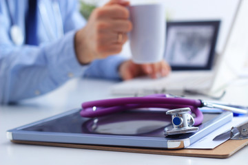 Doctor man with medical stethoscope sitting at the desk in the office and using laptop