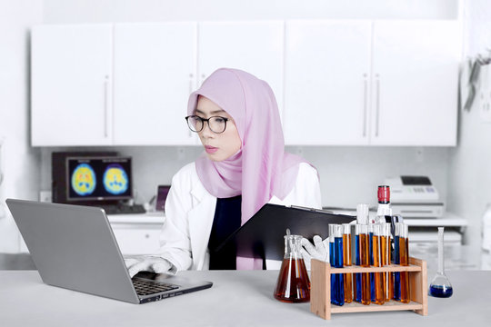 Muslim chemist with laptop and clipboard