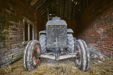  The front of a vintage tractor in an old brick barn with straw floor
