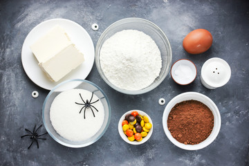 Halloween cookies with chocolate, orange and yellow candy. Raw baking ingredients for preparation cookies on dark stone background