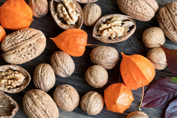 Whole and broken walnuts, physalis and autumn leaves on wooden background