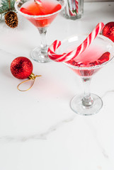 Christmas drinks, pink peppermint martini cocktail with xmas decoration and candy cane sweet on white marble kitchen table, copy space