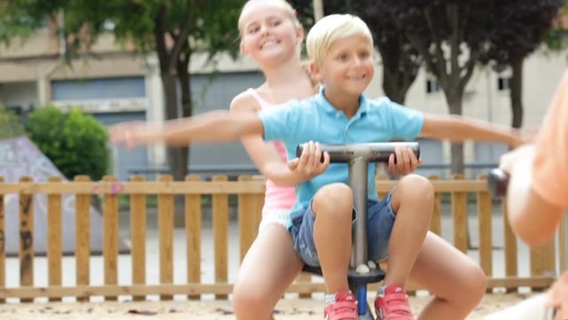 Company of kids are teetering on the swing on the playground
