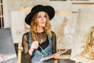 Female artist wears black hat posing near picture indoor the studio
