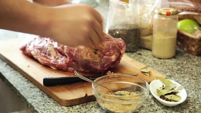 Hands of man add spices to the meat for preparing in oven
