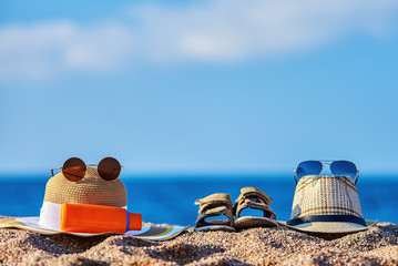 Family beach accessories. Father’s sunhat, mother’s bonnet hat, sandals of a child and bottle of sunscreen against the sea.