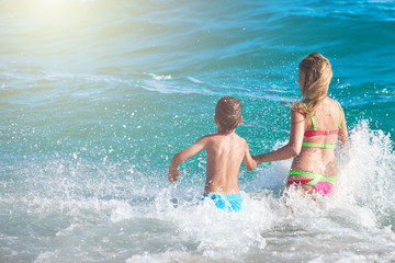 Caucasian mom and son running into the sea water. Back view.