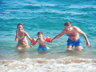 Family of three people getting out from the sea water together. Front view.