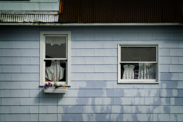 Fototapeta na wymiar Windows With Laundry Hanging Inside. A classic looking Alaskan house with a drying apron and other laundry with a planter box under the window.