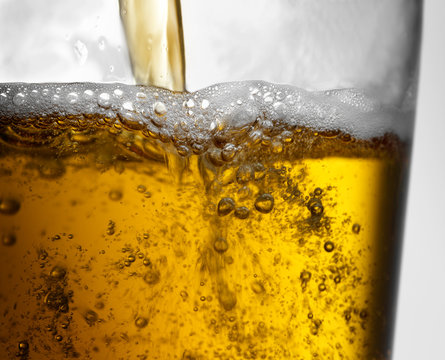 Closeup Of Beer Pour Action Into Clear Glass With Bubbles, Froth And Foam