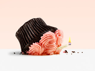 Accident, dropped cupcake with candle flame on a pink background