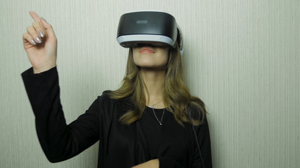 Woman using finger to touch on imaginary panel viewing on VR device against white wall. Girl use of vr device