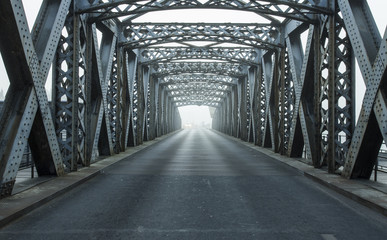 Metal construction of the city bridge on a foggy day in Dieppe, France. Empty asphalt road in the...