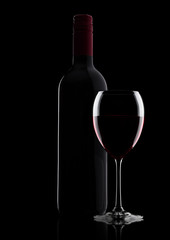 Glass of red wine with bottle with shape on black