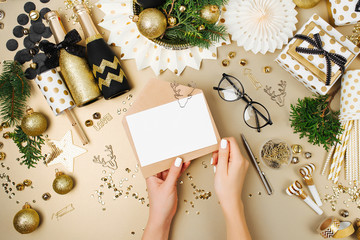 Fototapeta na wymiar Female hands hold mockup card and envelope. Christmas decoration background in golden and black colors. Flat lay, top view