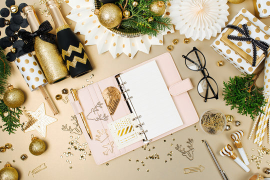 Open planner or notebook on desk with Christmas decoration background in golden and black colors. Flat lay, top view