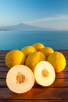 Typical mediterranean fruits: yellow melon with blue sea and Mount Etna in the background