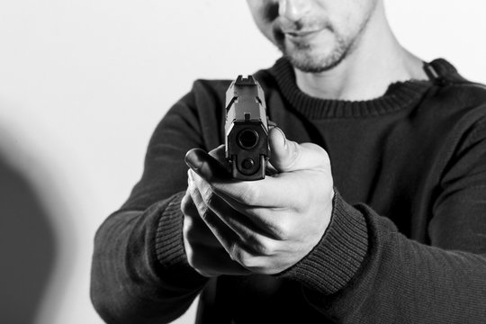 Man holding a pistol, aiming to the camera. Converted to black and white, grain added.