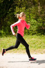 Young woman in pink and black dress runs cross country on a warm spring day
