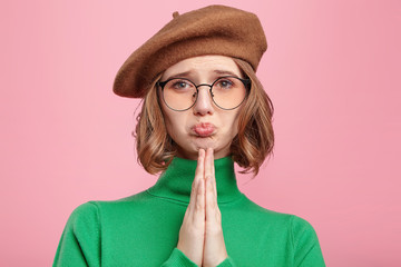 Beautiful woman wears old fashionable clothes, keeps palms pressed together in front of her, pouts...