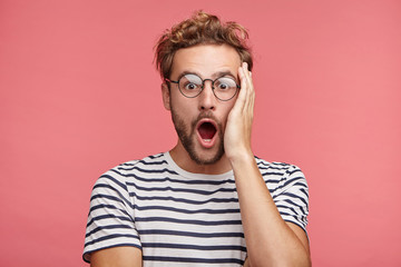Stupefied emotional shocked attractive fashionable man keeps hand on head, forgets to pay for...