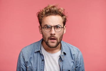 Curious scrupulous male model with trendy hairrdo and beard looks attentively at one point, sees something strange or suspicious. Angry man tries to overhear wife`s talk, looks annoyed, feels jealous