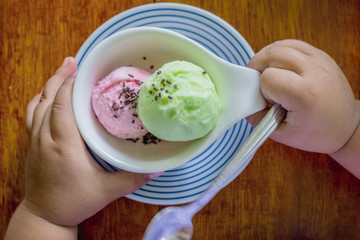 top view green and pink ice-cream in white cup with children's hands hold a spoon