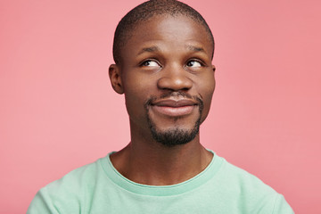 Isolated shot of pleasant looking male with dark skin has moony expression, looks aside up, dreams...