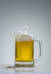 glass of beer with foam splashing on a gray background